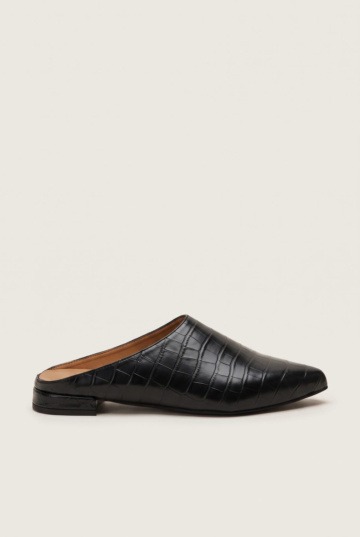 Side view of a single black croc-embossed pointed toe mule with a low flat heel and dark sole