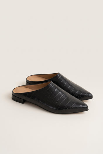 Angled view of a pair of black croc-embossed pointed toe mules with open backs and low flat heels