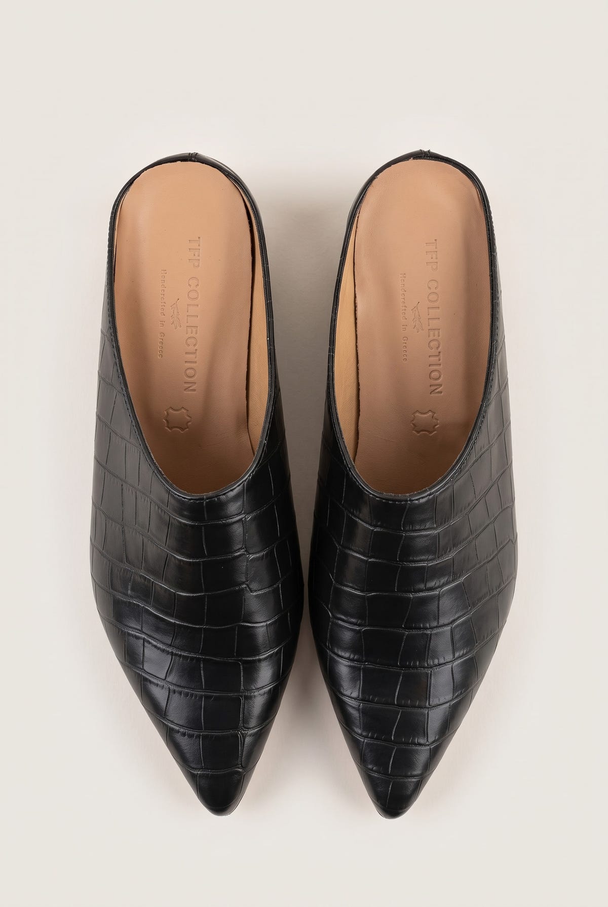 Top view of a pair of black croc-embossed pointed toe mules with tan leather insoles