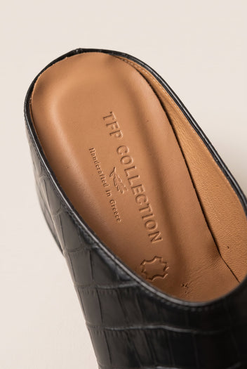 Close-up of a black croc-embossed mule showing the tan leather insole and rounded pointed toe