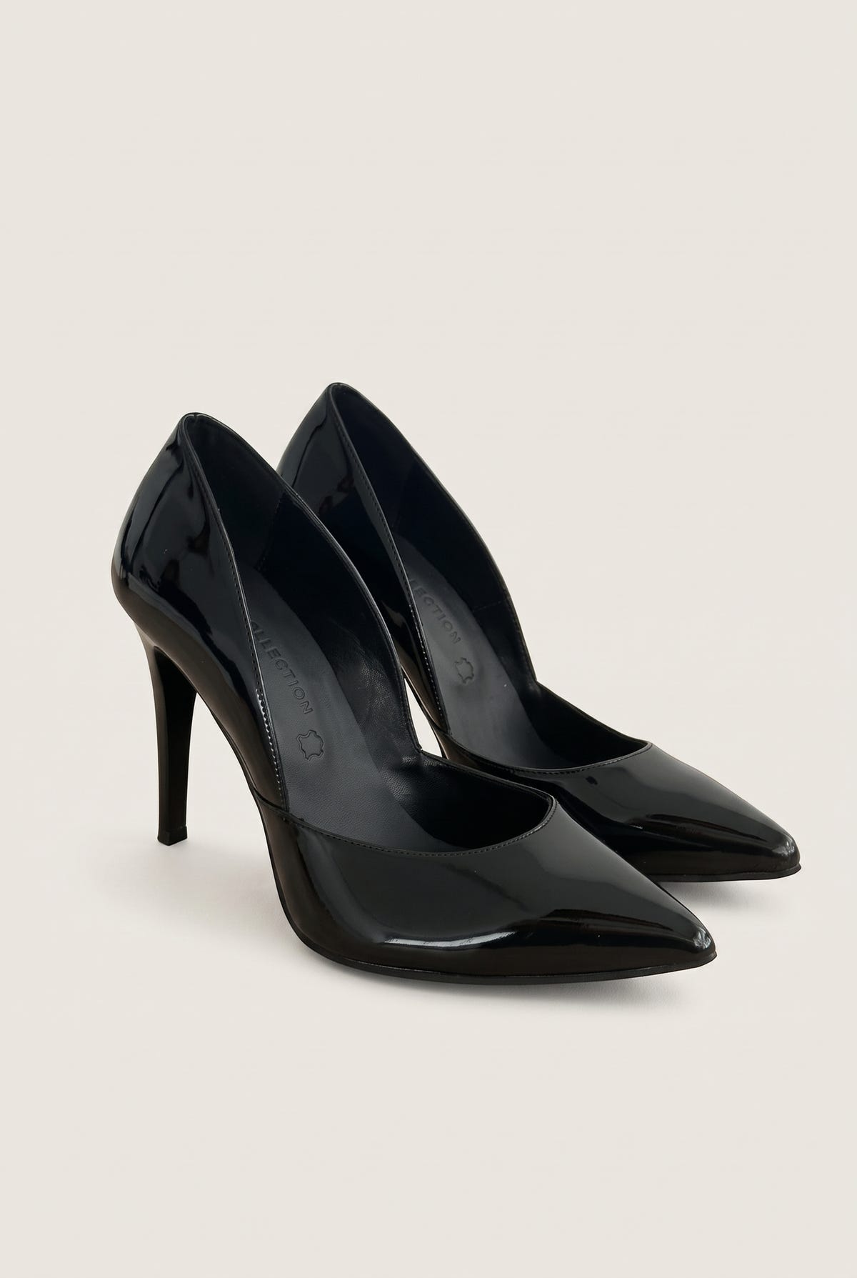 Pair of black patent pointed-toe pumps at an angle showing both cut-away sides and glossy finish on pale beige