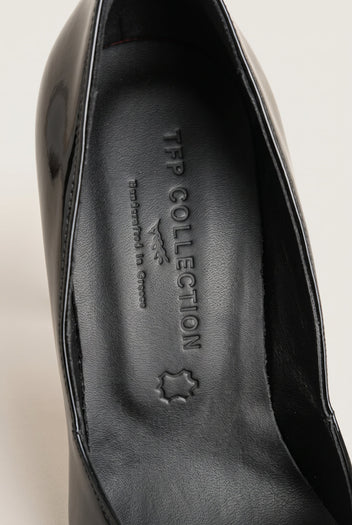 Close-up of a black patent pump interior with smooth leather insole and glossy curved edge of the upper