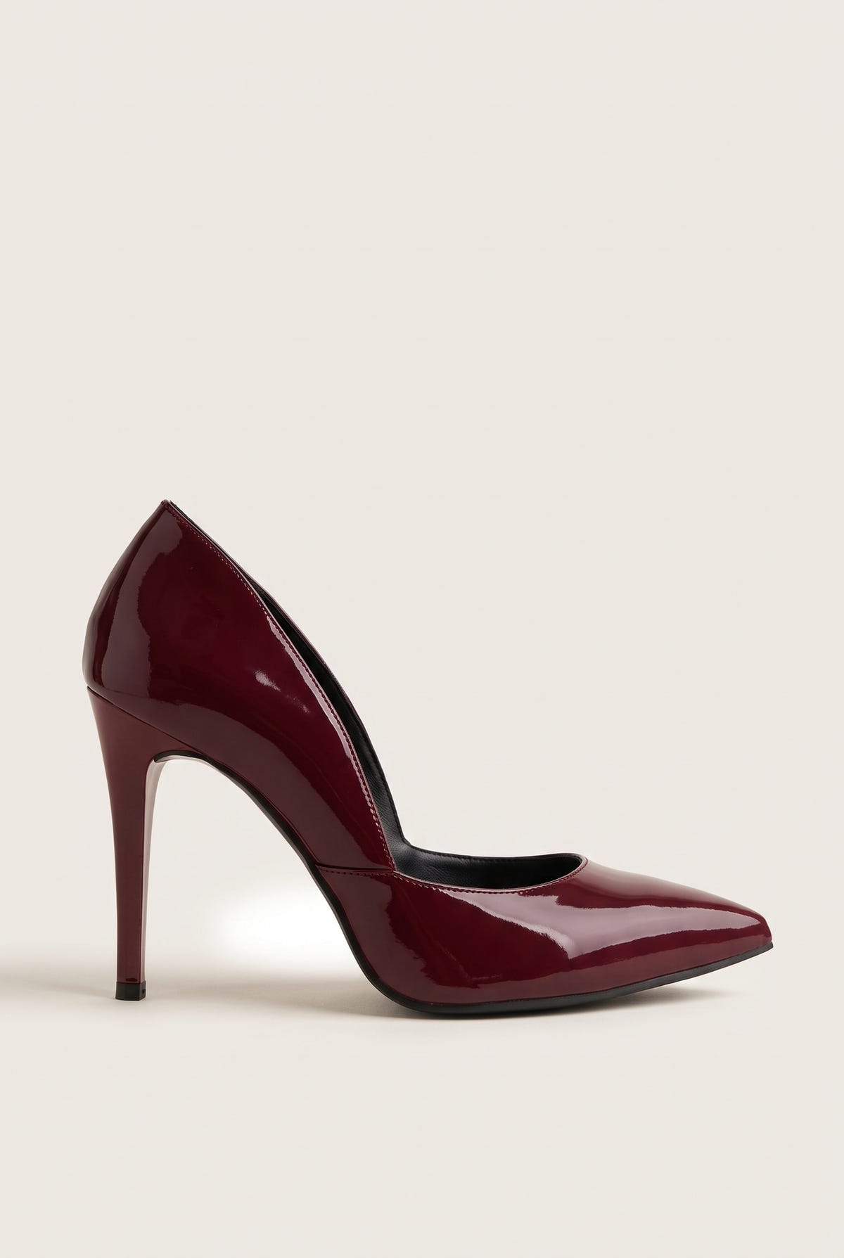 Side view of a bordeaux red patent pointed-toe pump with a cut-away side and a tall slim heel on pale beige