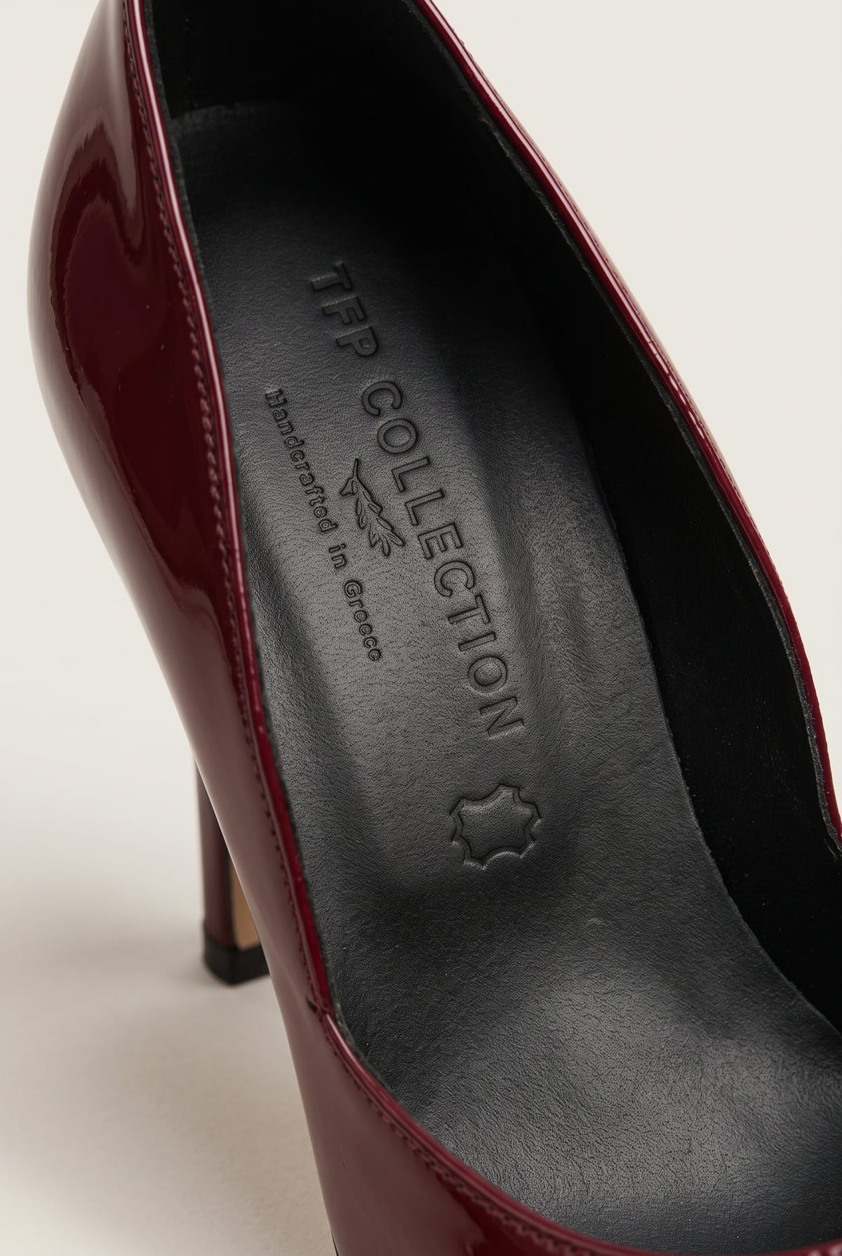 Close-up of a bordeaux patent pump interior with dark leather insole and glossy wine-red edge of the upper