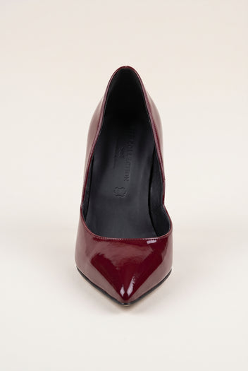 Front view of a bordeaux red patent pointed-toe pump with a narrow toe and glossy finish on a pale beige surface