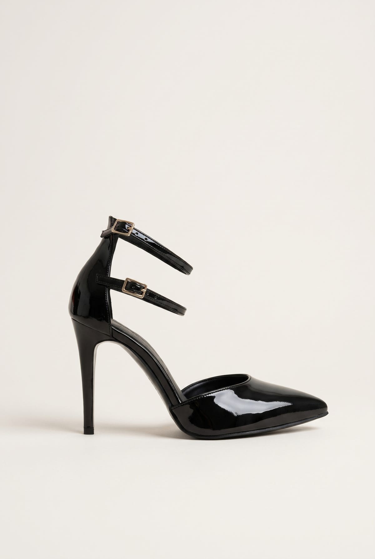 Black patent pointed toe pump with double ankle straps and thin stiletto heel in side view on a light surface