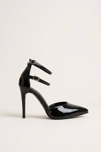 Black patent pointed toe pump with double ankle straps and thin stiletto heel in side view on a light surface
