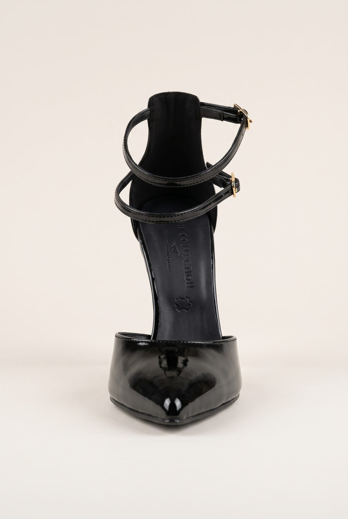 Front view of black patent pump showing the pointed toe box and crossed ankle straps with buckle