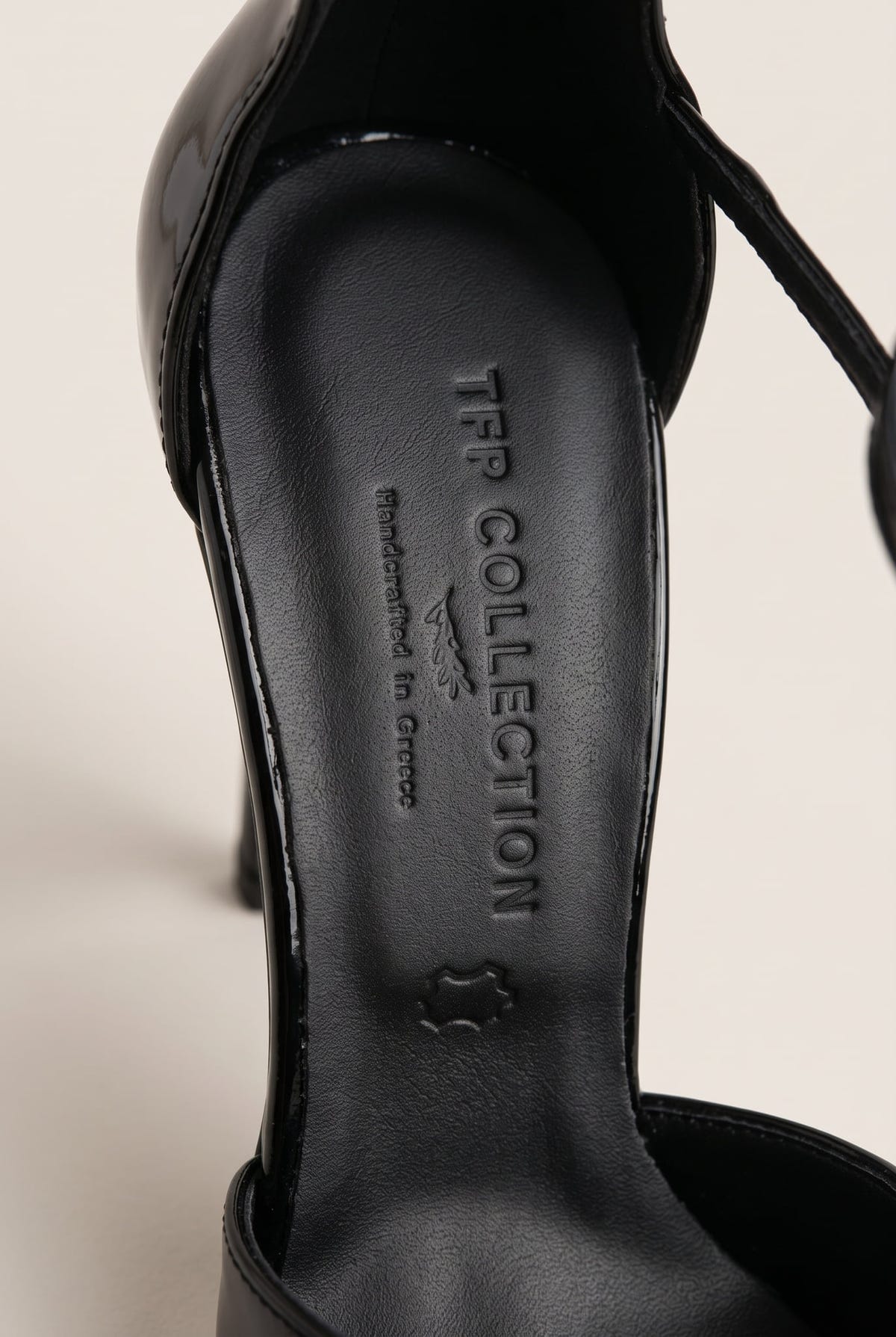 Close-up of the black insole and padded heel counter inside a black patent pump with a thin strap