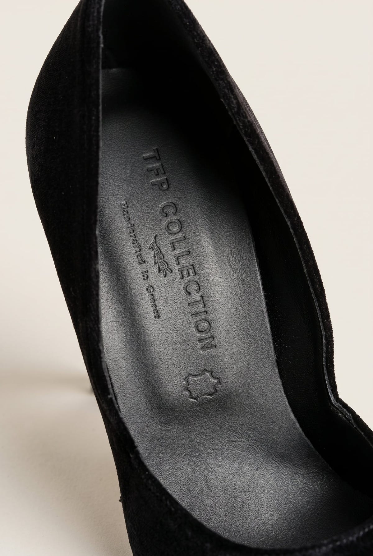 Close-up of a black velvet pump with a gold metal toe cap and a dark leather insole inside