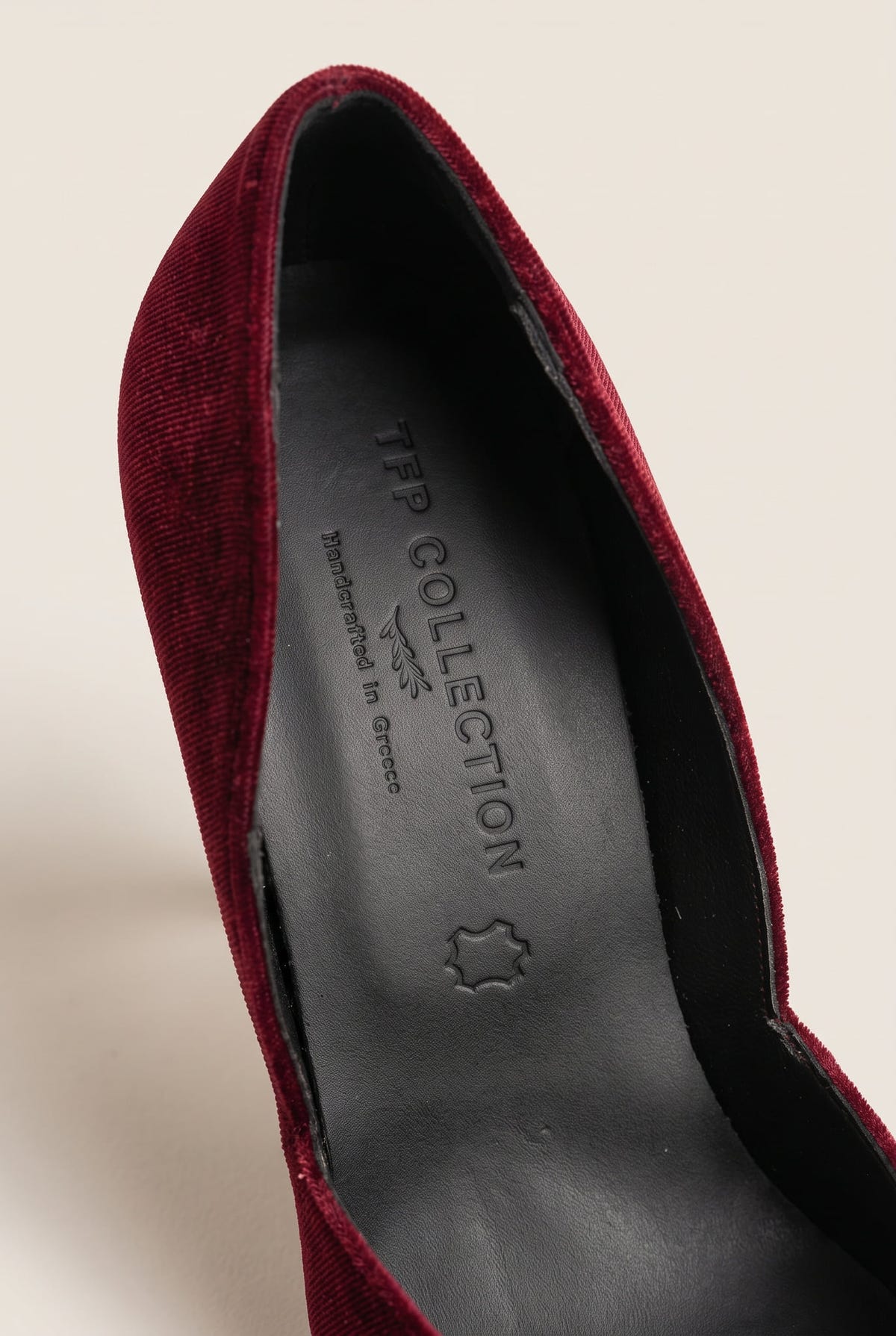 Close-up of bordeaux velvet upper curving along a dark leather insole inside the pump