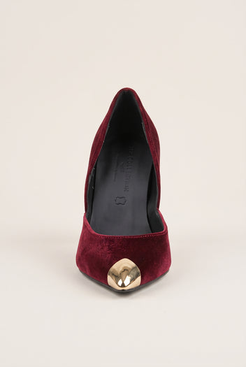 Front view of a bordeaux velvet pump showing the pointed toe with a gold metal cap on pale beige