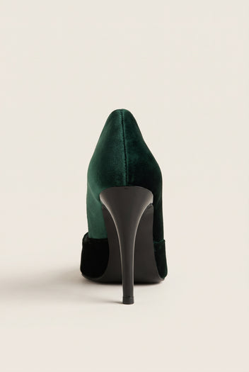 Back view of a dark green velvet pump with a tall slim heel and black heel counter on pale beige