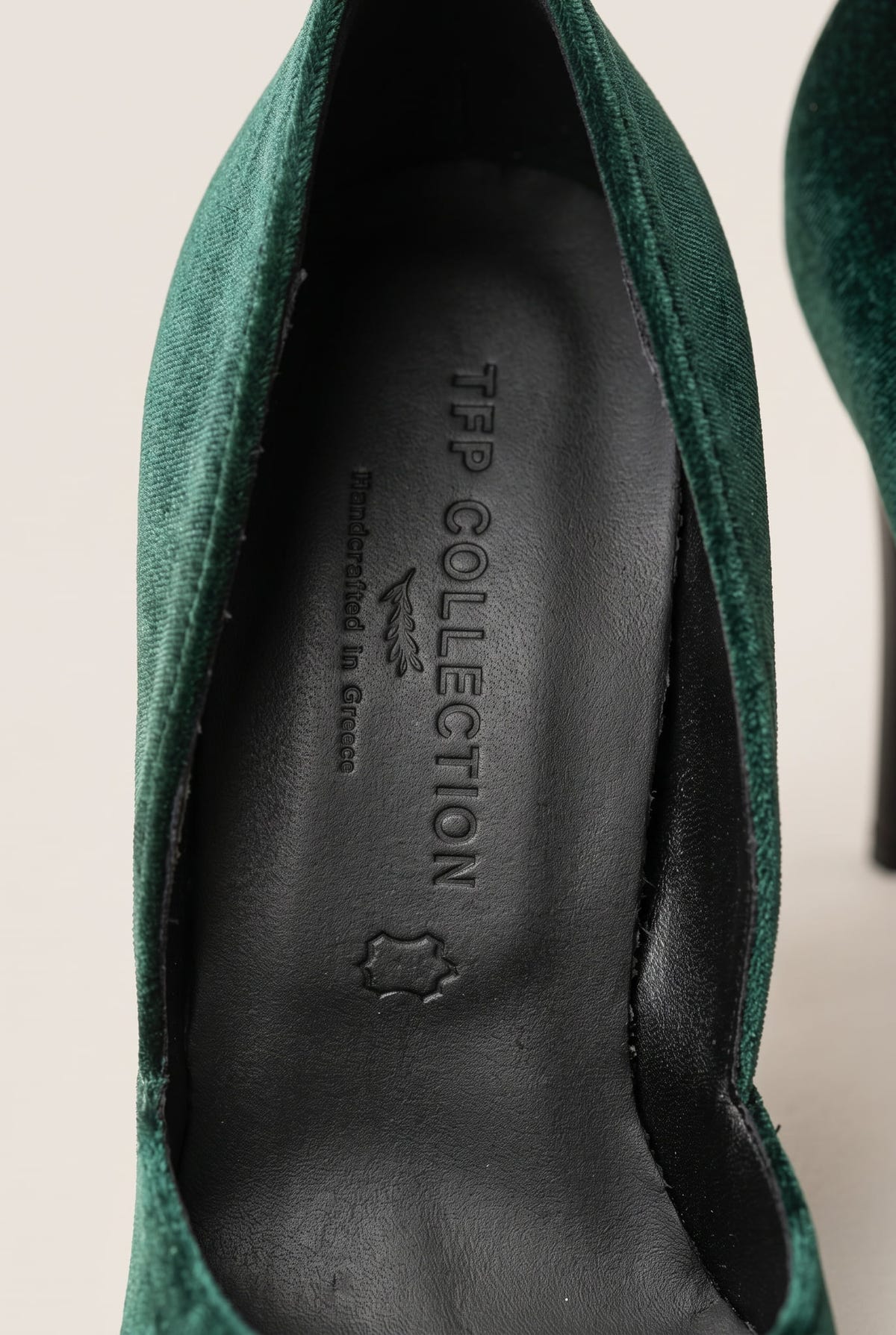 Close-up of a dark green velvet pump with the upper edge curving along a dark leather insole