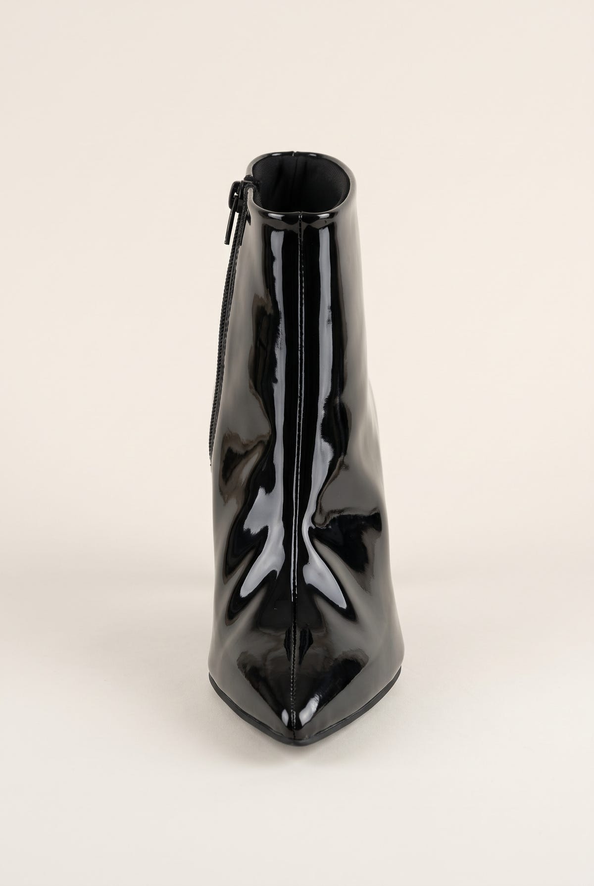 Front view of black patent ankle boot with pointed toe facing forward and a narrow zip at the top edge