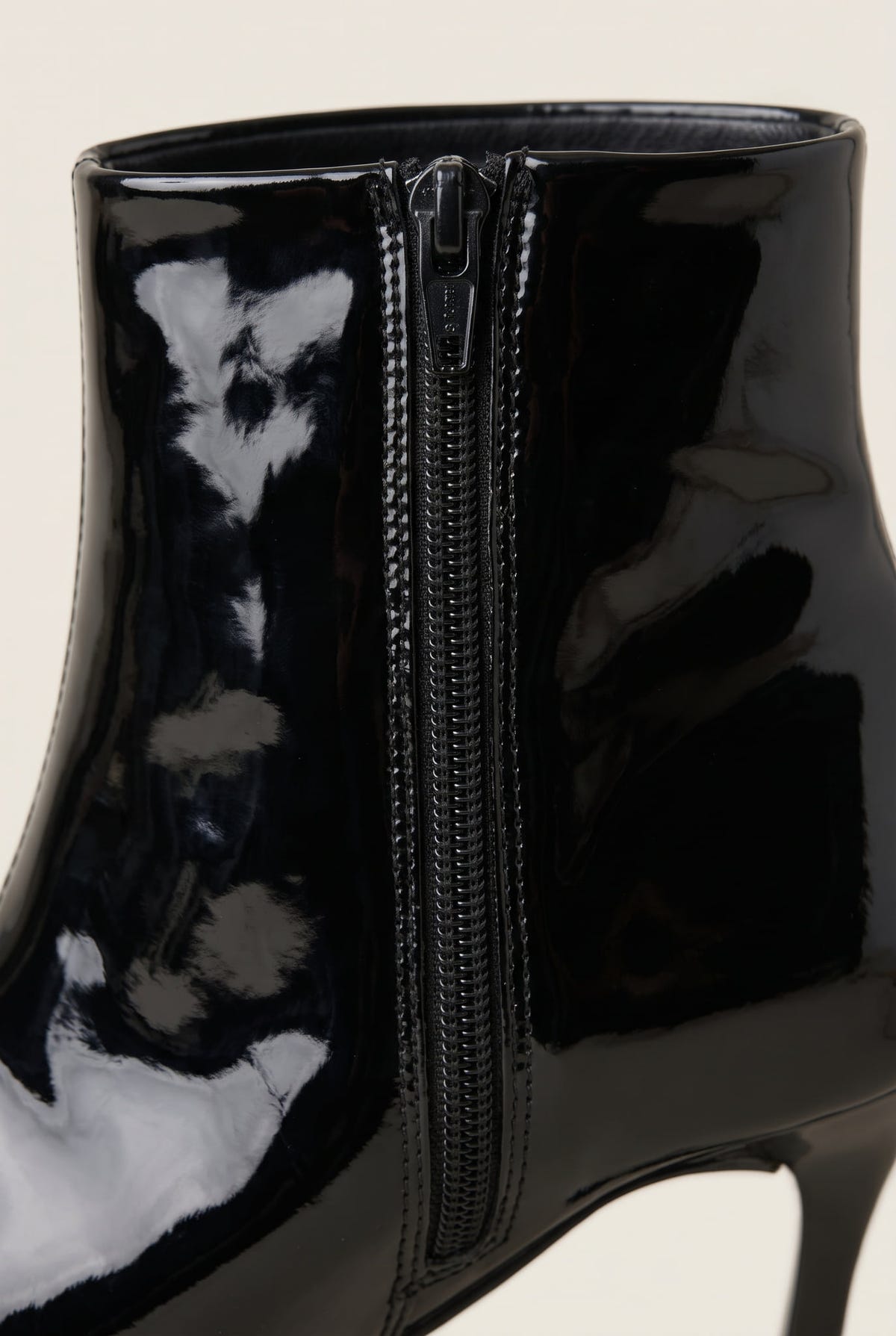 Close-up of black patent ankle boot showing the glossy finish and side zip running up the back of the shaft