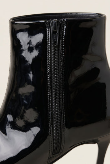 Close-up of black patent ankle boot showing the glossy finish and side zip running up the back of the shaft