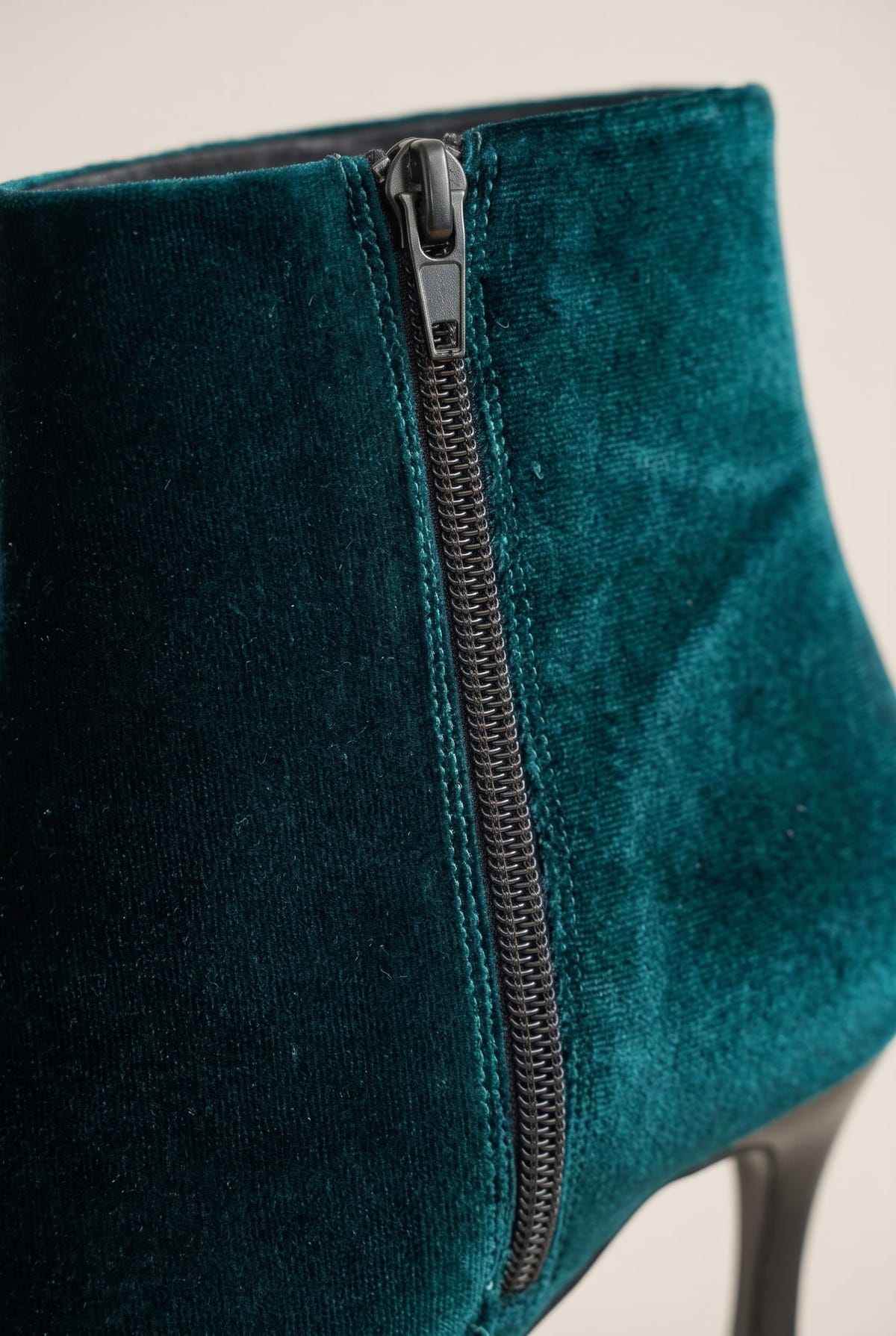 Close-up of dark green velvet ankle boot showing the zip, soft pile texture and heel edge
