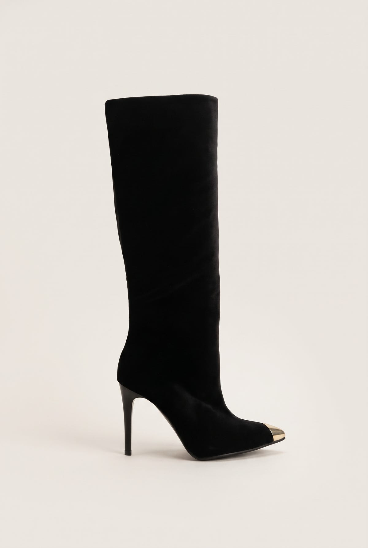 Black velvet knee high pointed toe boot with gold tone metal toe cap and stiletto heel in side view