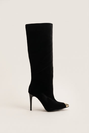 Black velvet knee high pointed toe boot with gold tone metal toe cap and stiletto heel in side view