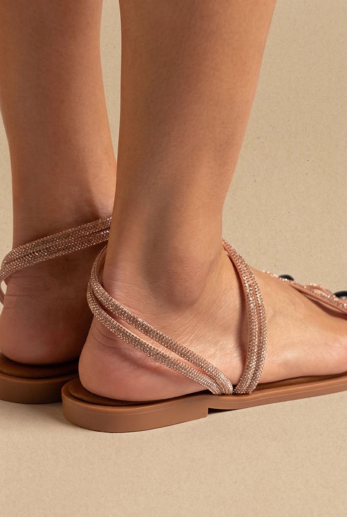 Close-up side view of model ankle with thin copper strappy sandal wrapping around the ankle