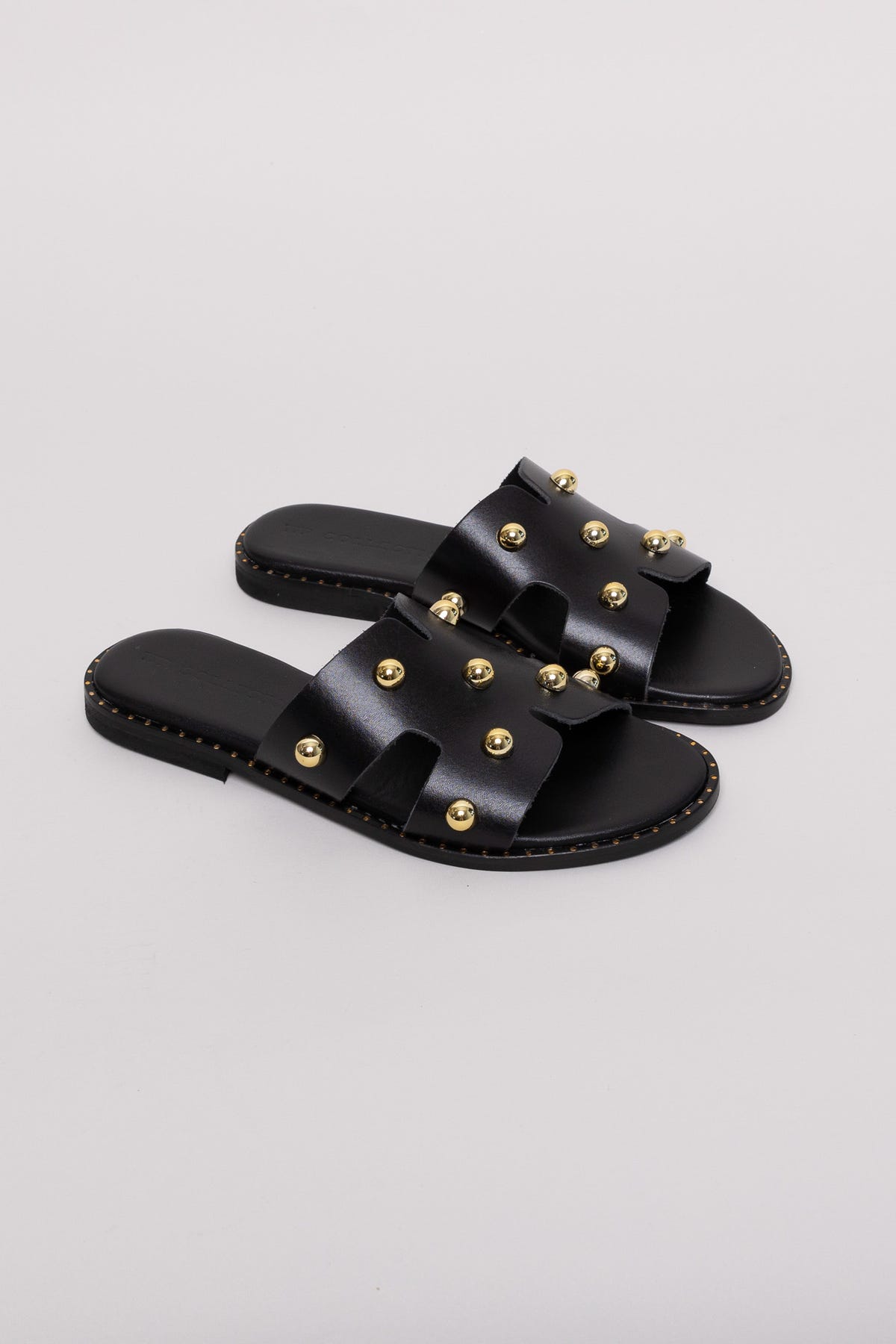 Black leather studded slide sandals with gold studs, angled view on a terracotta backdrop