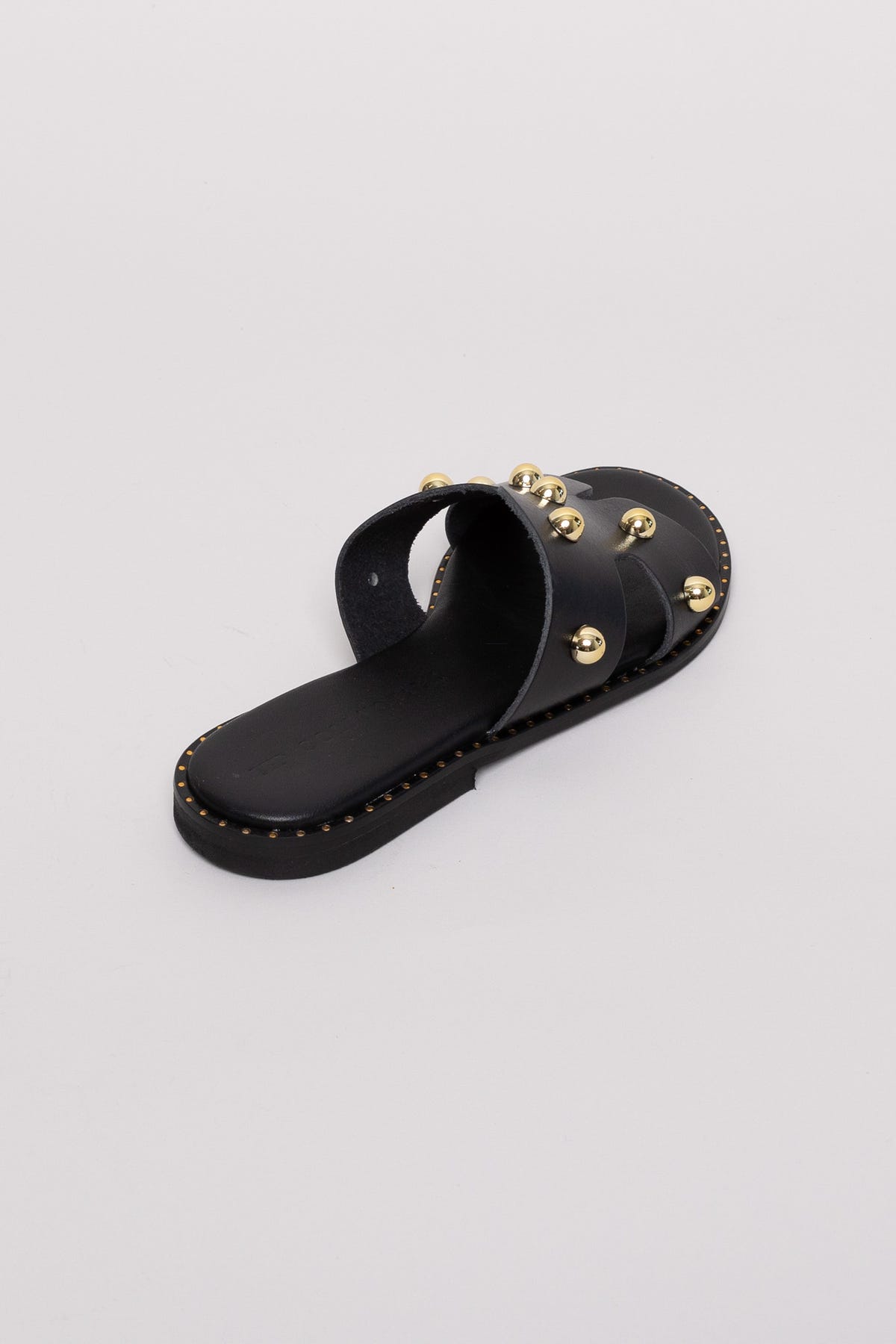 Black leather studded slide sandals with gold studs, angled view on grey background