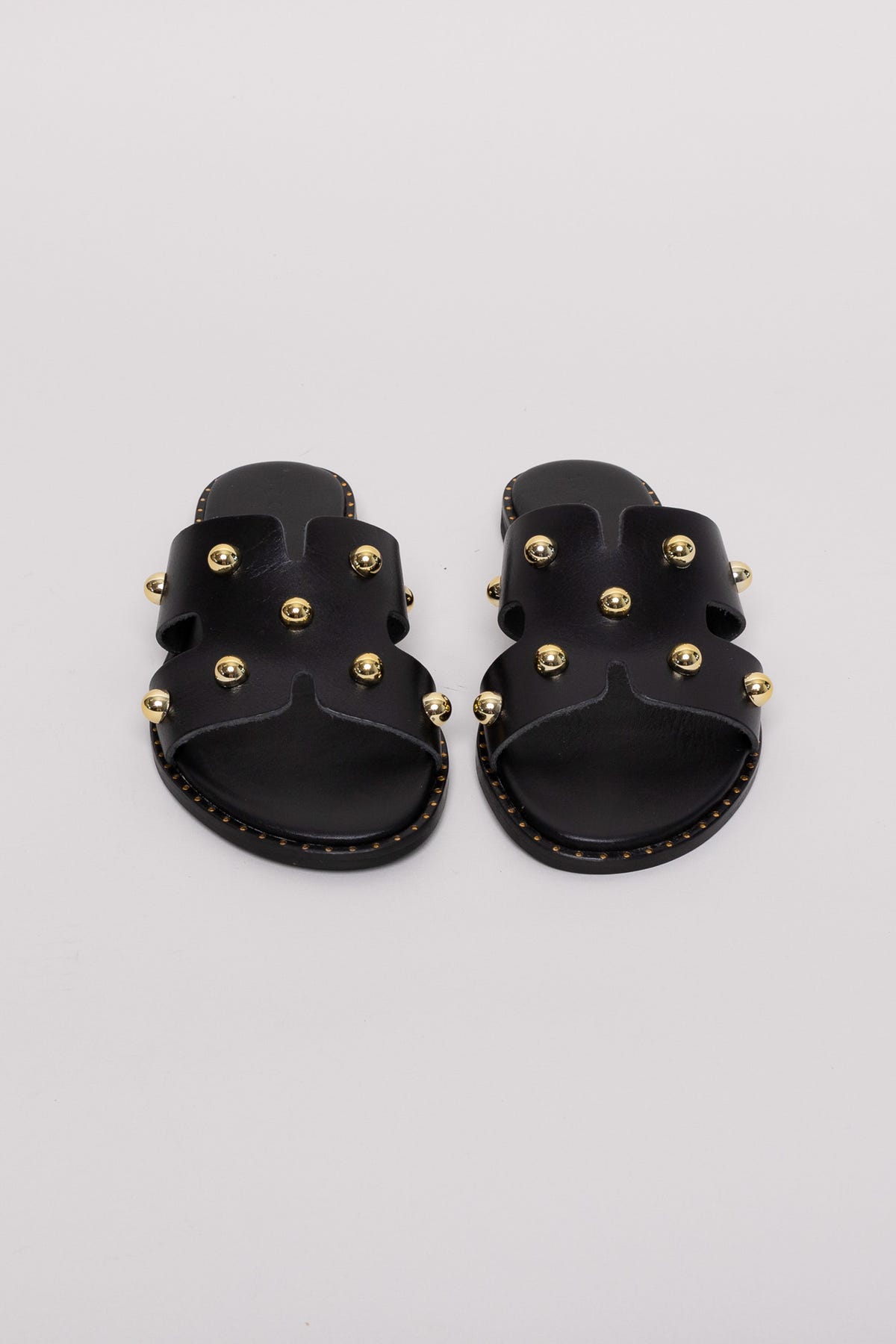 Black leather studded slide sandals with gold studs, pair view on grey background