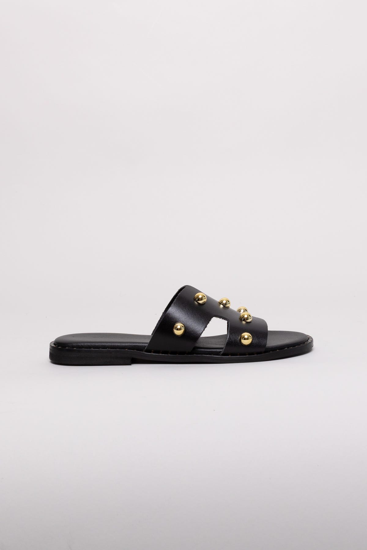 Black leather slide sandal with gold stud detail and flat sole, angled view on a white background