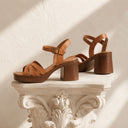 Brown leather sandals on a decorative white pedestal against a light background