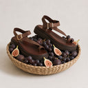 Brown sandals with gold buckles on a woven basket filled with grapes and figs.