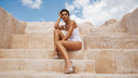 Woman sitting on stone steps with a clear blue sky and clouds in the background