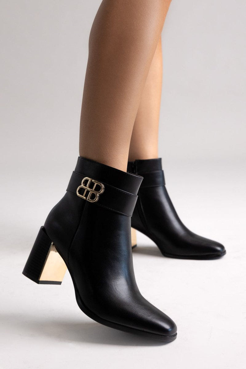 Black leather ankle boot with pointed toe and block heel, angled view on a model's legs in studio light