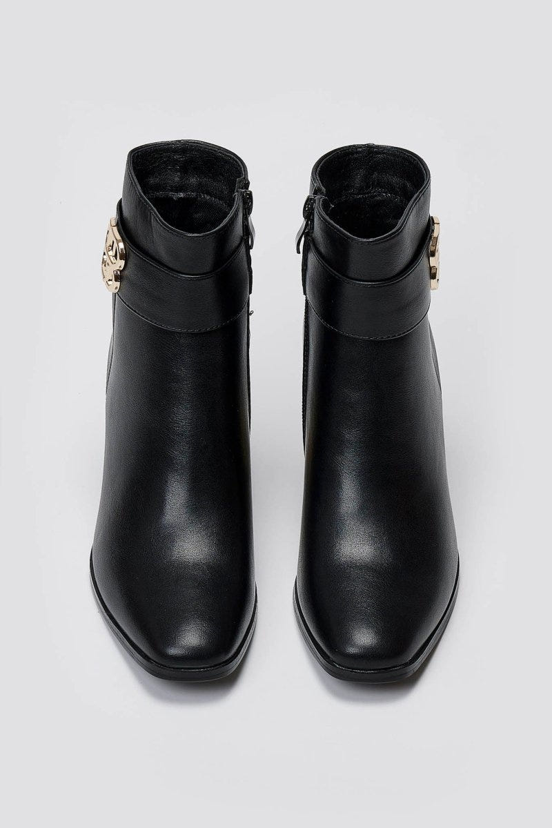 Black leather ankle boots with block heel and gold-tone logo buckle, pair in top-down view on a light grey background