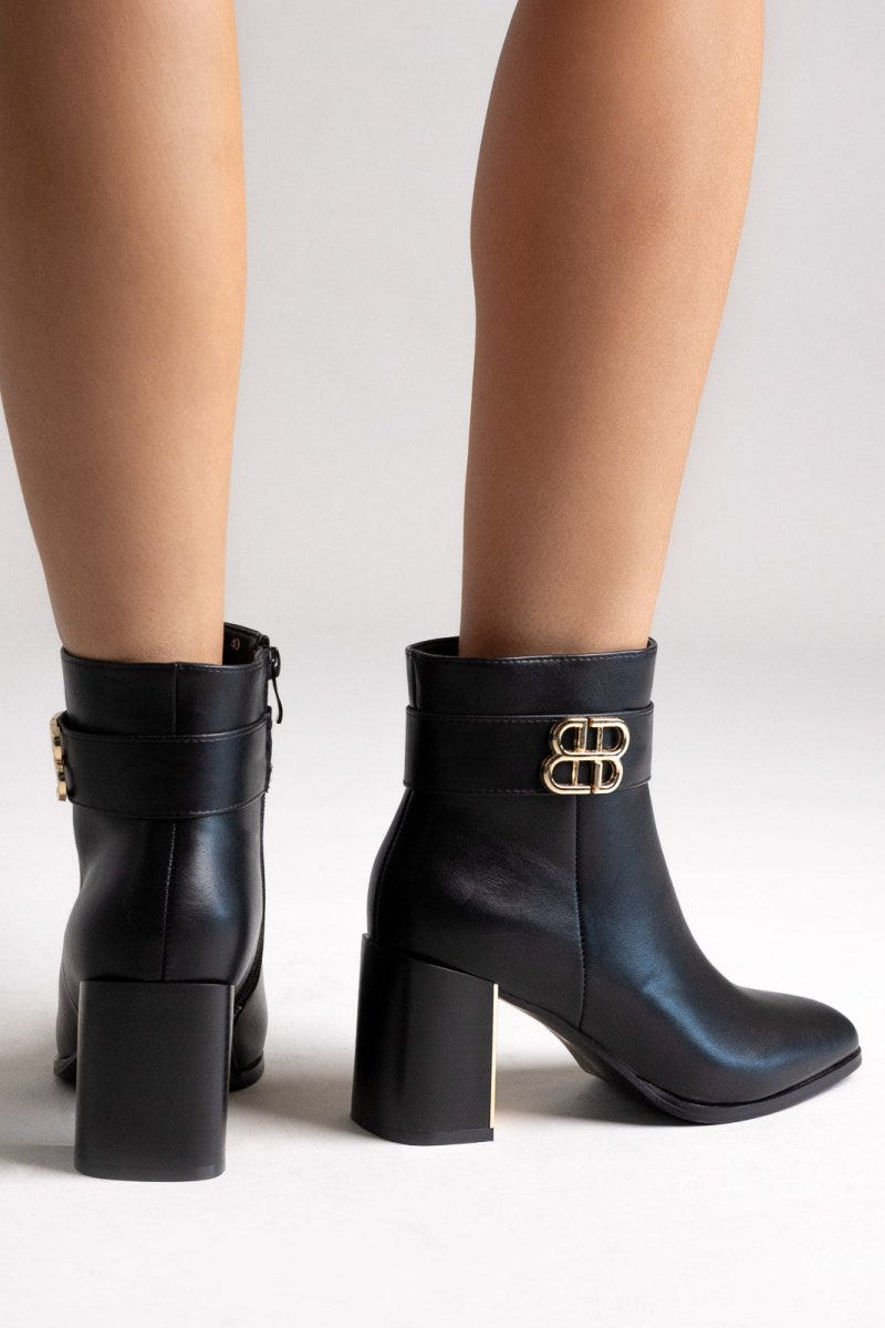 Black leather ankle boots with pointed toe and block heel, pair in angled view on a model's legs in studio light