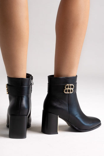 Black leather ankle boots with pointed toe and block heel, pair in angled view on a model's legs in studio light