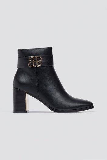 Black leather ankle boot with pointed toe, block heel and gold-tone logo buckle, angled view on a light grey background
