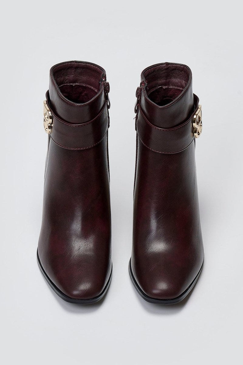 Burgundy leather ankle boots with block heel and gold-tone logo buckle, pair in top-down view on a light grey background