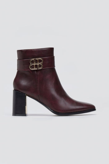 Burgundy leather ankle boot with block heel and gold-tone logo buckle, single boot in angled view on a light grey background