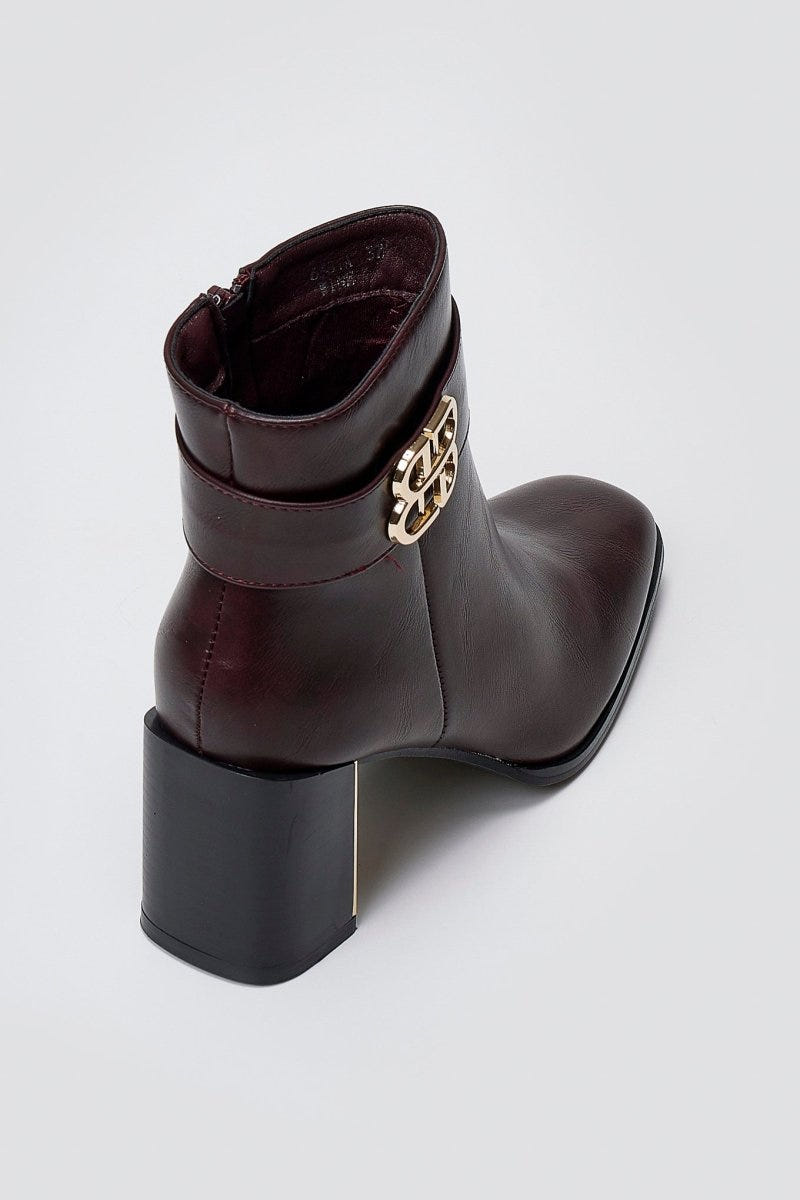 Burgundy leather ankle boot with block heel and gold-tone logo buckle, side view on a light grey background