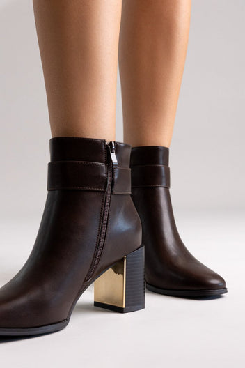 Dark brown leather ankle boot with block heel and side zip, angled view on a model's legs in studio light