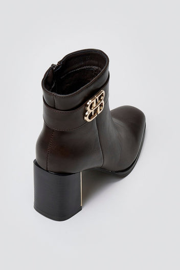Dark brown leather ankle boot with square toe, block heel and gold-tone logo buckle, angled view on a light grey background