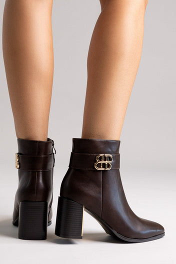 Dark brown leather ankle boots with block heel and gold-tone logo buckle, pair in front view on a model's legs in studio light