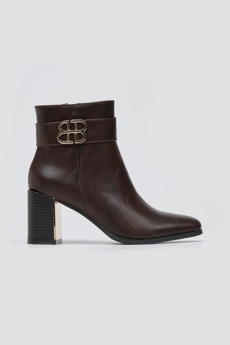Dark brown leather ankle boot with block heel and gold-tone logo buckle, angled view on a light grey background