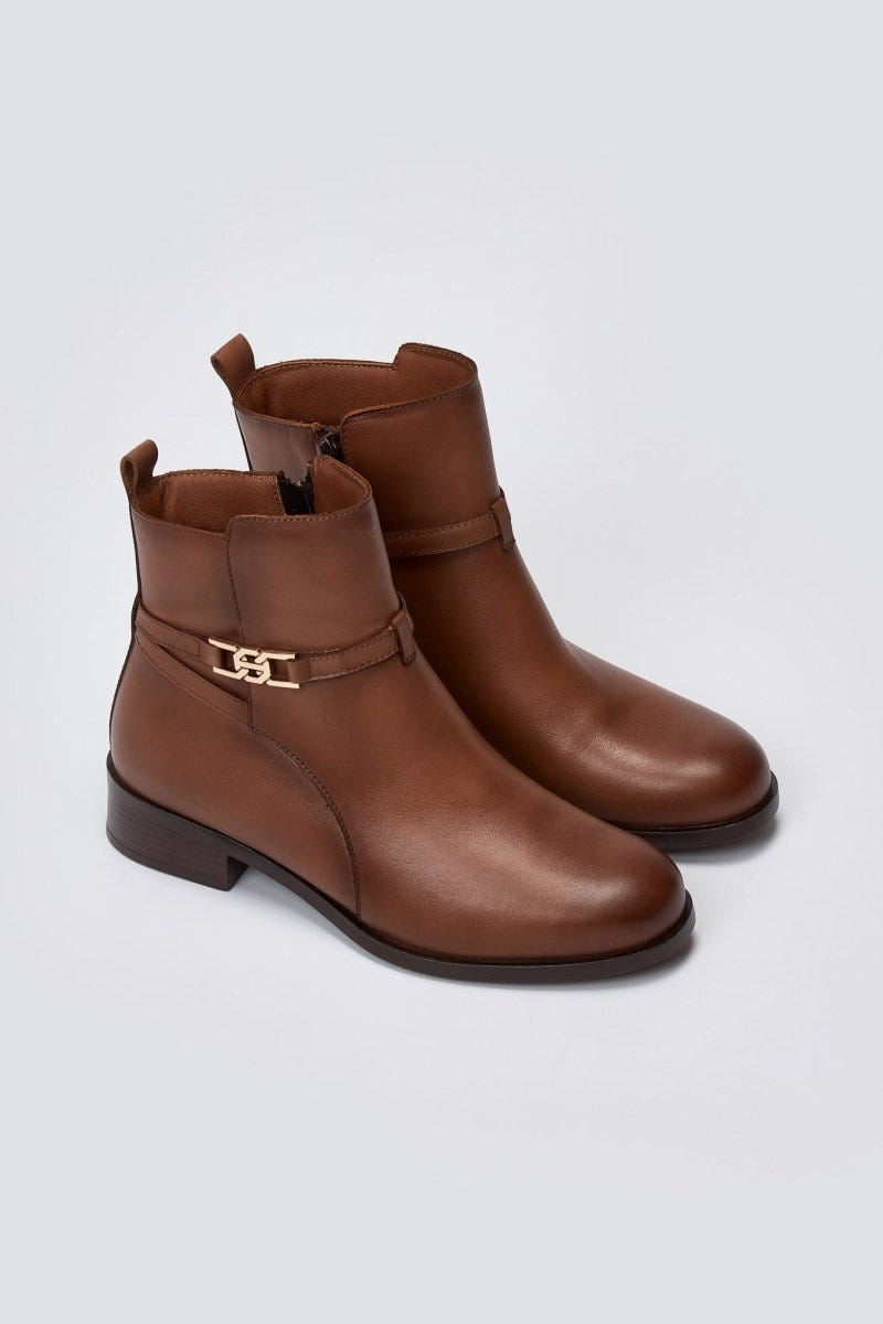 Brown leather ankle boots with flat heel and gold-tone logo buckle strap, pair in angled view on a light grey background