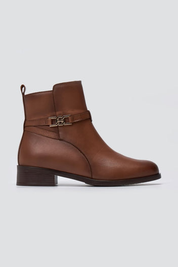 Brown leather ankle boot with low block heel and gold-tone logo buckle, side view on a light grey background