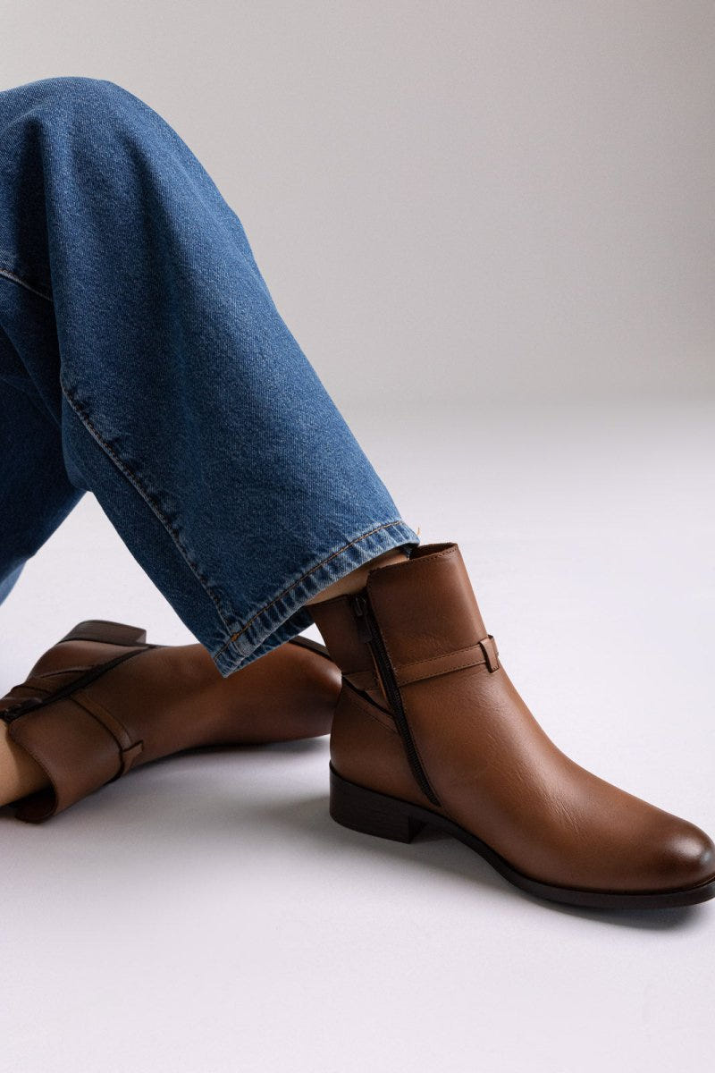 Brown leather ankle boot with low block heel and gold-tone buckle strap, pair in side view on a model's legs in studio light