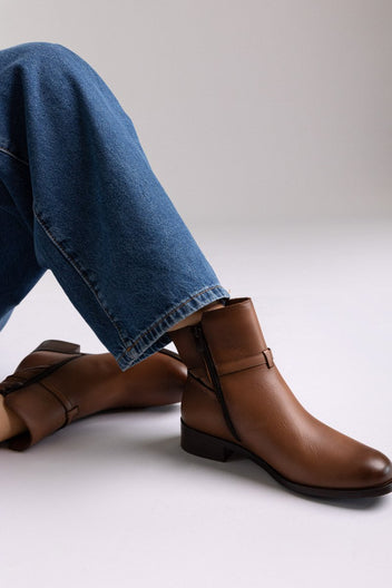Brown leather ankle boot with low block heel and gold-tone buckle strap, pair in side view on a model's legs in studio light