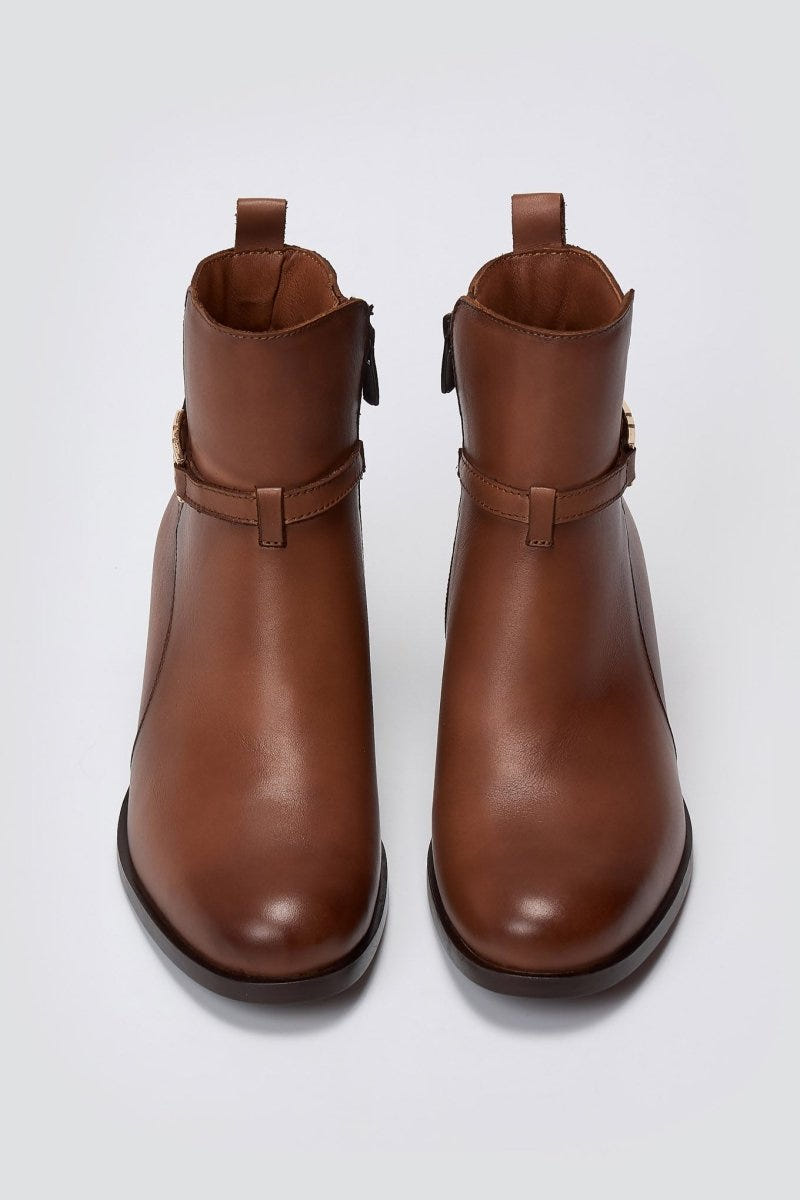 Brown leather ankle boots with pull tab and gold-tone buckle strap, pair in top-down view on a light grey background