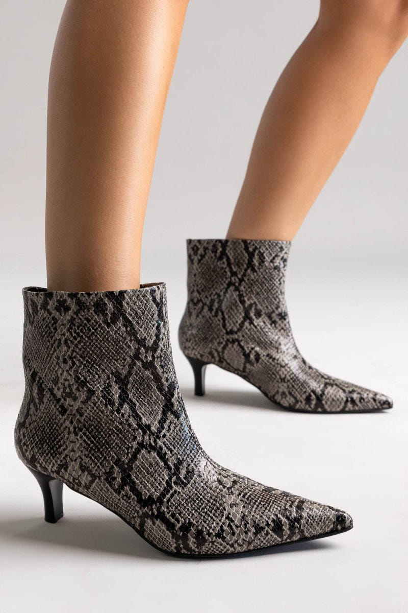 Grey snake-embossed leather ankle boots with pointed toe and kitten heel, pair in angled view on a model's legs in studio light